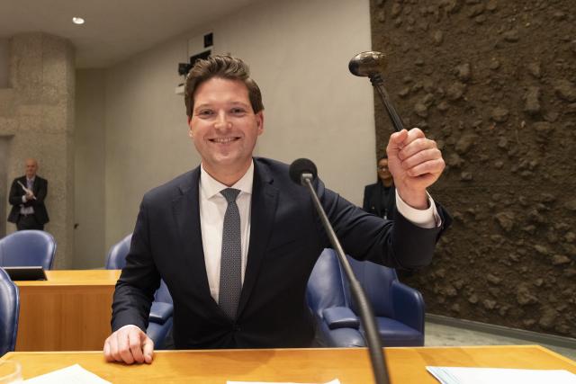 Thom van Campen zit op de stoel van de Voorzitter en houdt de Voorzittershamer vast.