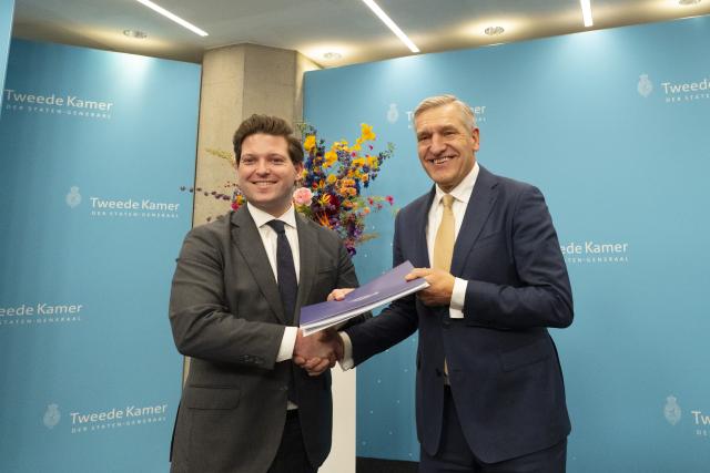 Thom van Campen (links) en Sybrand Buma staan naast elkaar, ze houden samen een document vast en schudden elkaar de hand. 