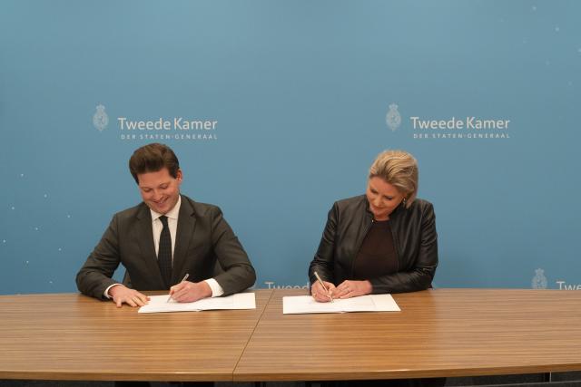 Kamervoorzitter Thom van Campen en informateur Rianne Letschert ondertekenen een document zittend aan een tafel.