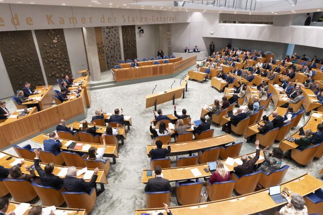 De plenaire zaal van de Tweede Kamer. De zaal is gevuld met Kamerleden. Een deel van hen steekt de hand op.