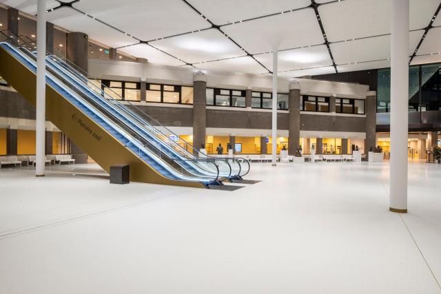Grote hal met pilaren. Op de voorgrond twee roltrappen.