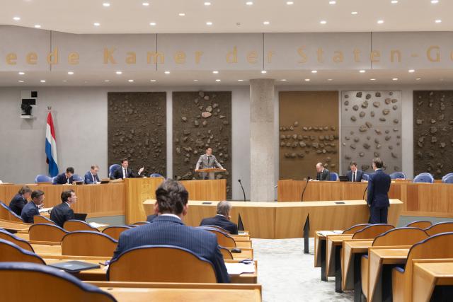 Kamerlid Henk-Jan Oosterhuis staat achter het spreekgestoelte in de plenaire zaal van de Tweede Kamer. Naast hem zit Kamervoorzitter Thom van Campen. In vak K zitten minister Eelco Heinen en Eelco Eerenberg.