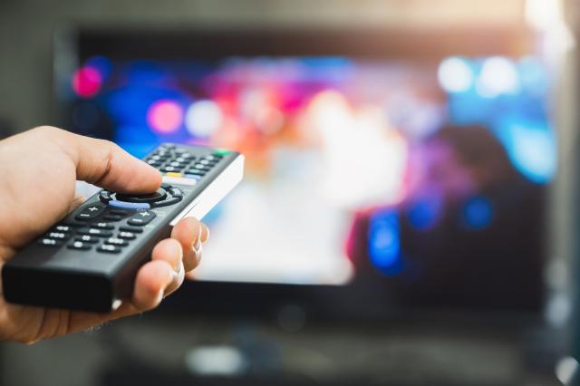 Hand met afstandsbediening. Op de achtergrond een televisiescherm dat vervaagd is.