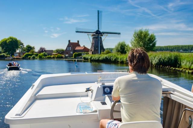 Een man vaart in een bootje. Op de achtergrond zie je een windmolen. 
